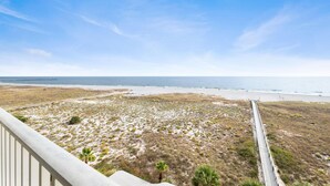 A coastal landscape with a paved road leading to the beach, a clear sky, and sparse vegetation. - Tidewater 503 (Orange Beach)