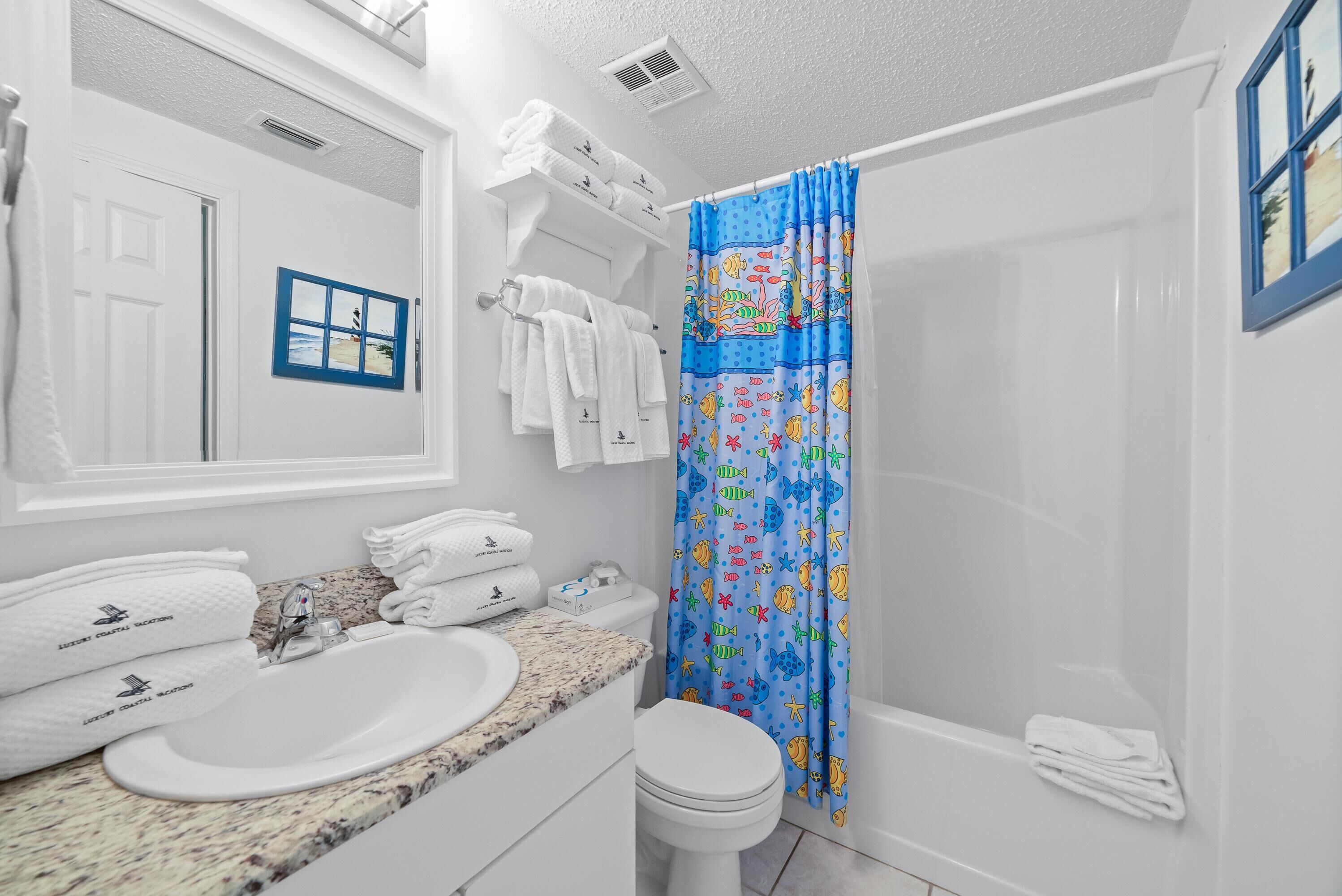 A bathroom with a white sink, a toilet, and a shower curtain with a fish pattern.