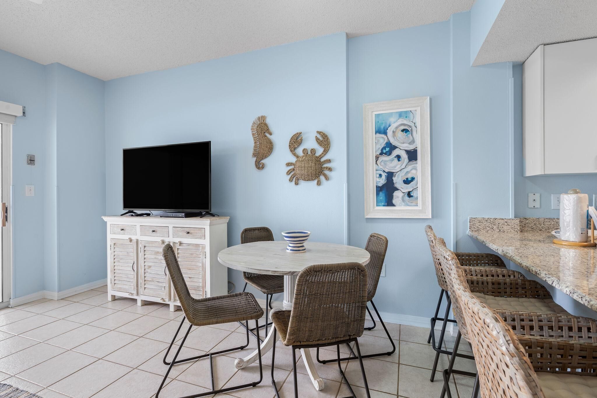 A dining area with a round table, wicker chairs, a flat-screen TV, and decorative wall art.
