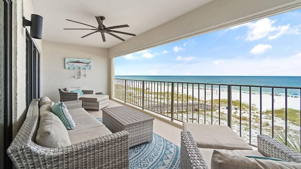 A balcony with wicker furniture, a ceiling fan, and a view of the beach. - Shipwatch A403 (Pensacola)