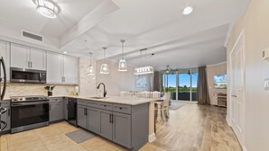 A modern kitchen with grey cabinets, a central island, stainless steel appliances, pendant lighting, and a view to a balcony. - Lost Key B304 (Pensacola)