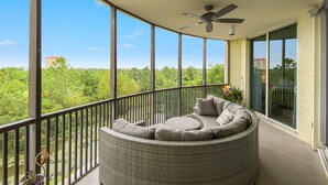 A balcony with a wicker sofa, a ceiling fan, and a view of greenery. - Lost Key B304 (Pensacola)