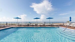 A pool area with clear blue water, sun loungers, and blue umbrellas. - Lost Key B304 (Pensacola)