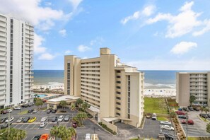 A beachfront hotel with multiple floors, a parking lot, and a pool area.