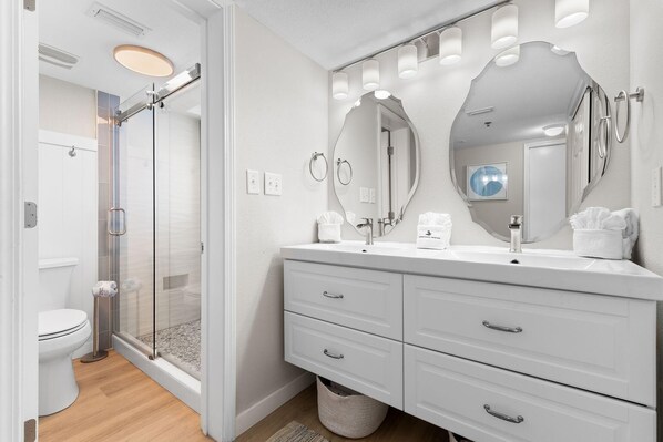 A modern bathroom with a glass shower enclosure, white vanity with a large mirror, and a toilet.