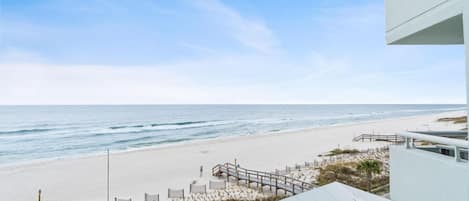 A beach view with a wooden walkway leading to the shore, a sandy beach, and a clear sky.