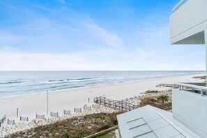 A beach view with a wooden walkway leading to the shore, a sandy beach, and a clear sky.