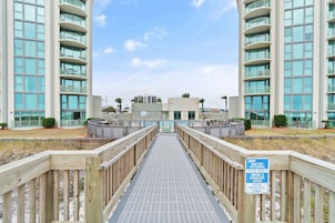 A wooden walkway leading to a modern building with balconies and large windows.