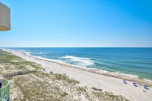 A beach view with a clear sky, sandy beach, and a few umbrellas.