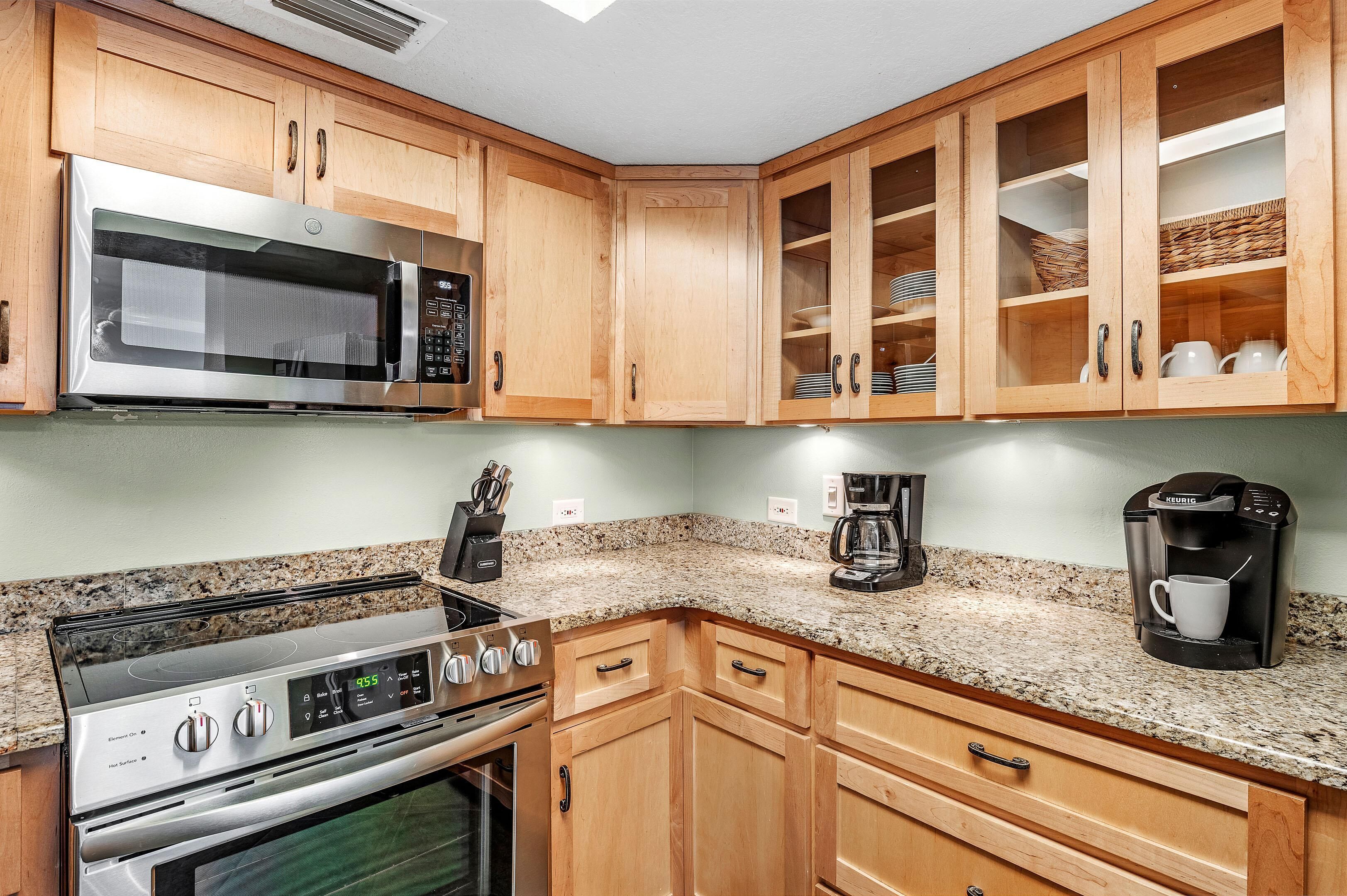 A kitchen with wooden cabinets, a stainless steel microwave, a stove, and a coffee maker.