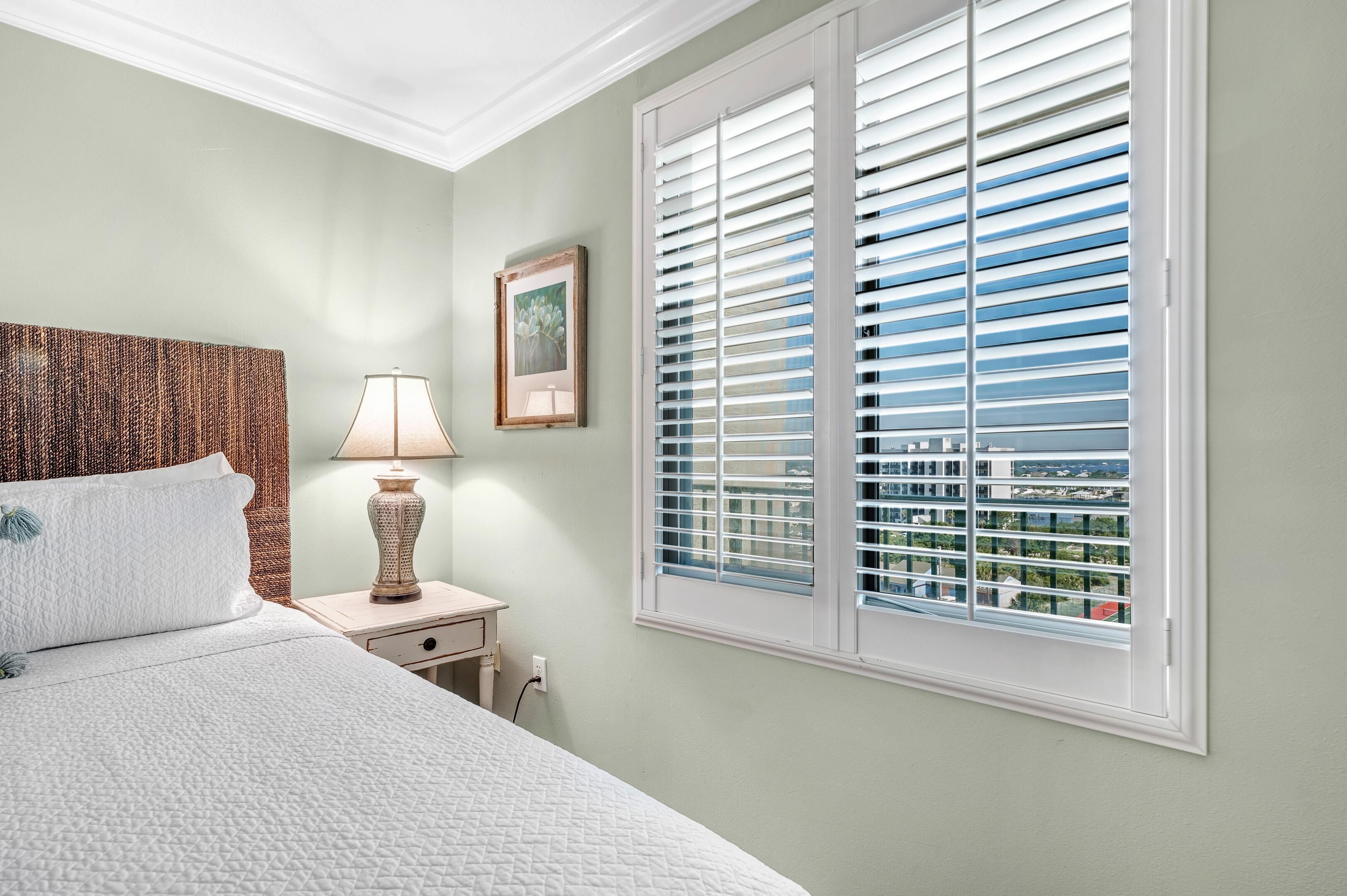 A bedroom with a bed, nightstand, lamp, and window with blinds.