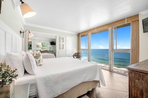 A bedroom with a large bed, a view of the ocean, and a sliding door to a balcony.