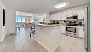 A modern kitchen with white cabinets, a central island, stainless steel appliances, and a view to the living area. - Spanish Key 510 (Pensacola)