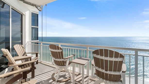 Ein Balkon mit zwei Adirondack-Stühlen und einem kleinen Tisch, mit Blick auf den Ozean.