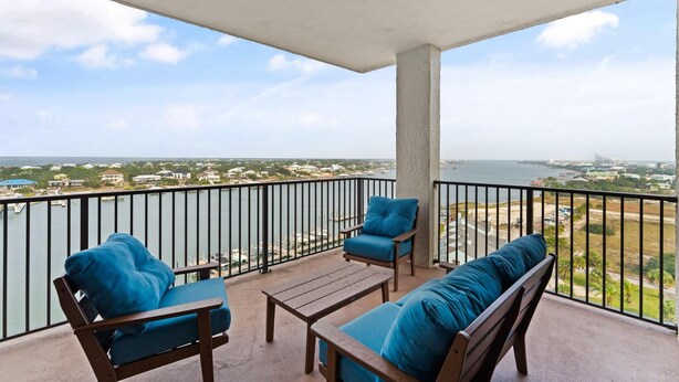 A balcony with a view of a body of water, a cityscape, and a bridge in the distance. - Shipwatch Riverside E1005 (Pensacola)