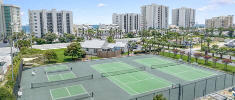 Un complexe de courts de tennis comprenant plusieurs terrains, entouré d’immeubles résidentiels et de palmiers.