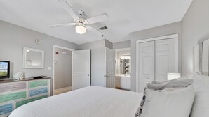 Ein Schlafzimmer mit einem großen Bett, einem Deckenventilator, einer Kommode mit bunten Schubladen und weißen Türen zu anderen Räumen.
