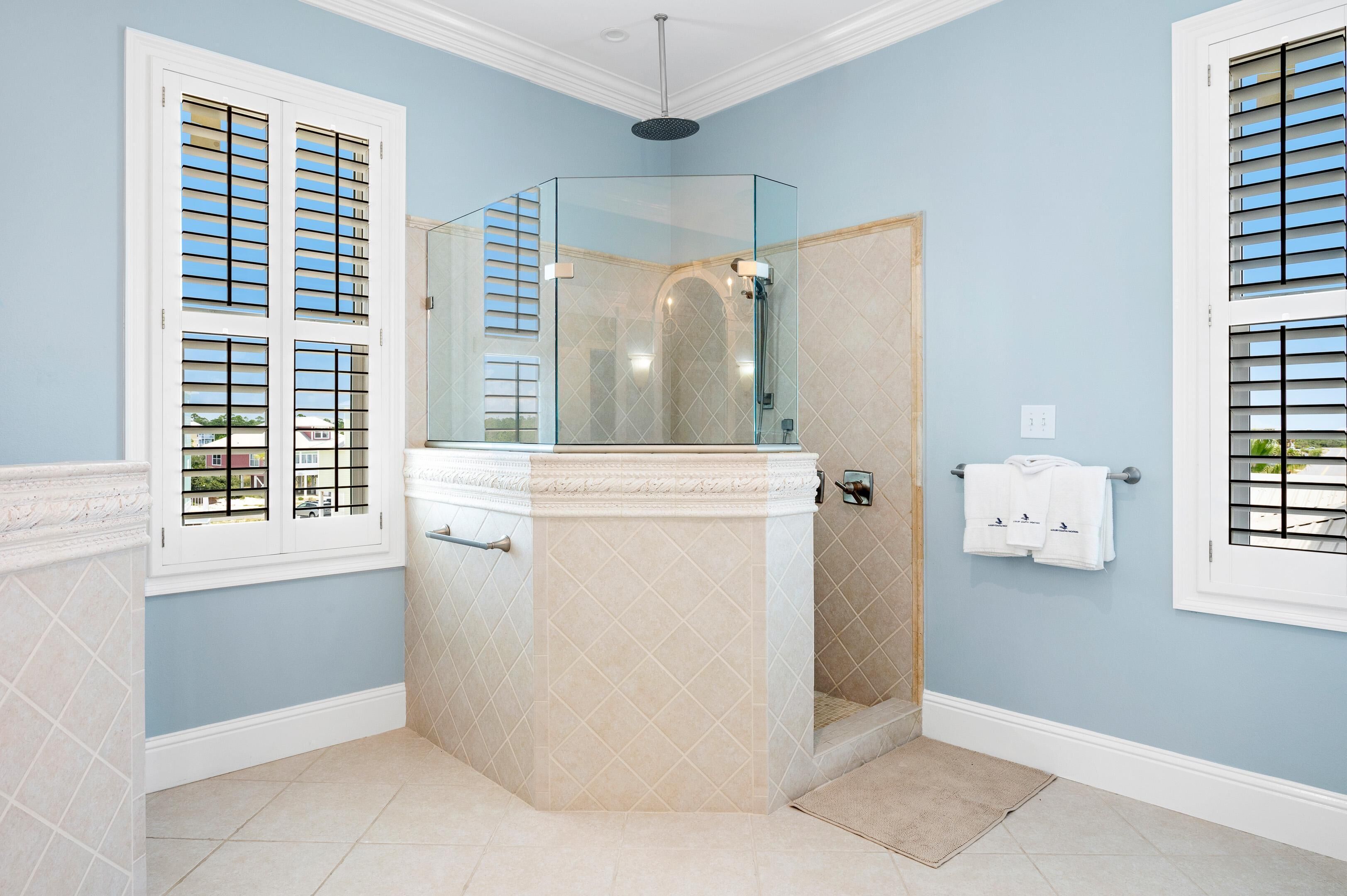 A bathroom with a glass-enclosed shower, a towel rack, and a window with blinds.