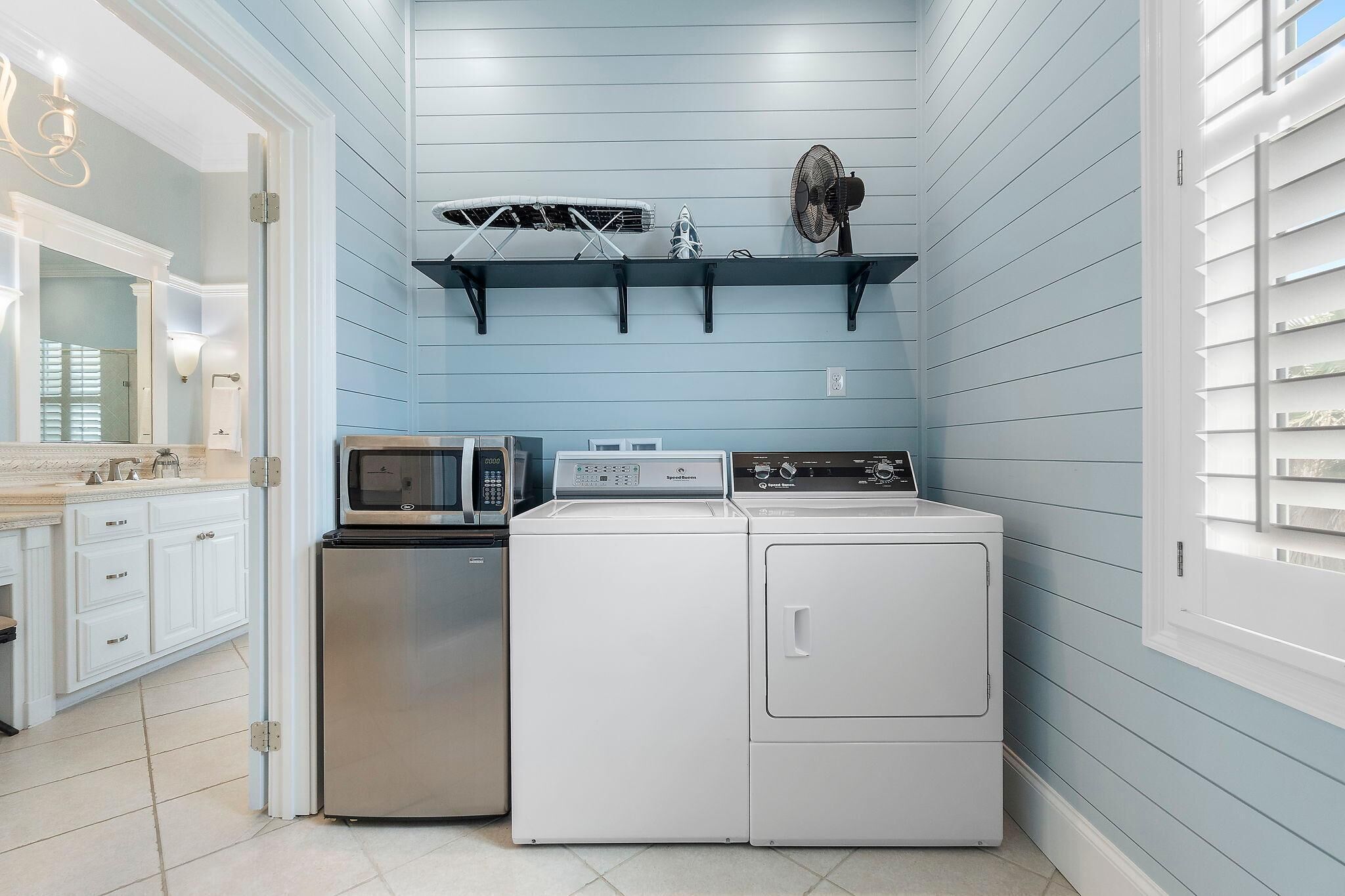 Une buanderie équipée d’un lave-linge, d’un sèche-linge, d’un four à micro-ondes et d’une étagère sur laquelle est posé un ventilateur.
