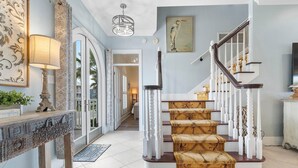 Un escalier avec des balustrades blanches et une main courante en bois, menant à un palier recouvert d’une moquette à motifs.