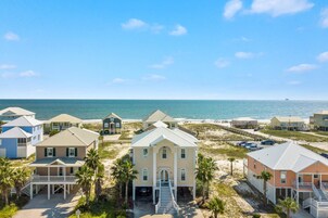 A coastal property with multiple houses, a central building with a staircase leading to a porch, and a beach in the background.