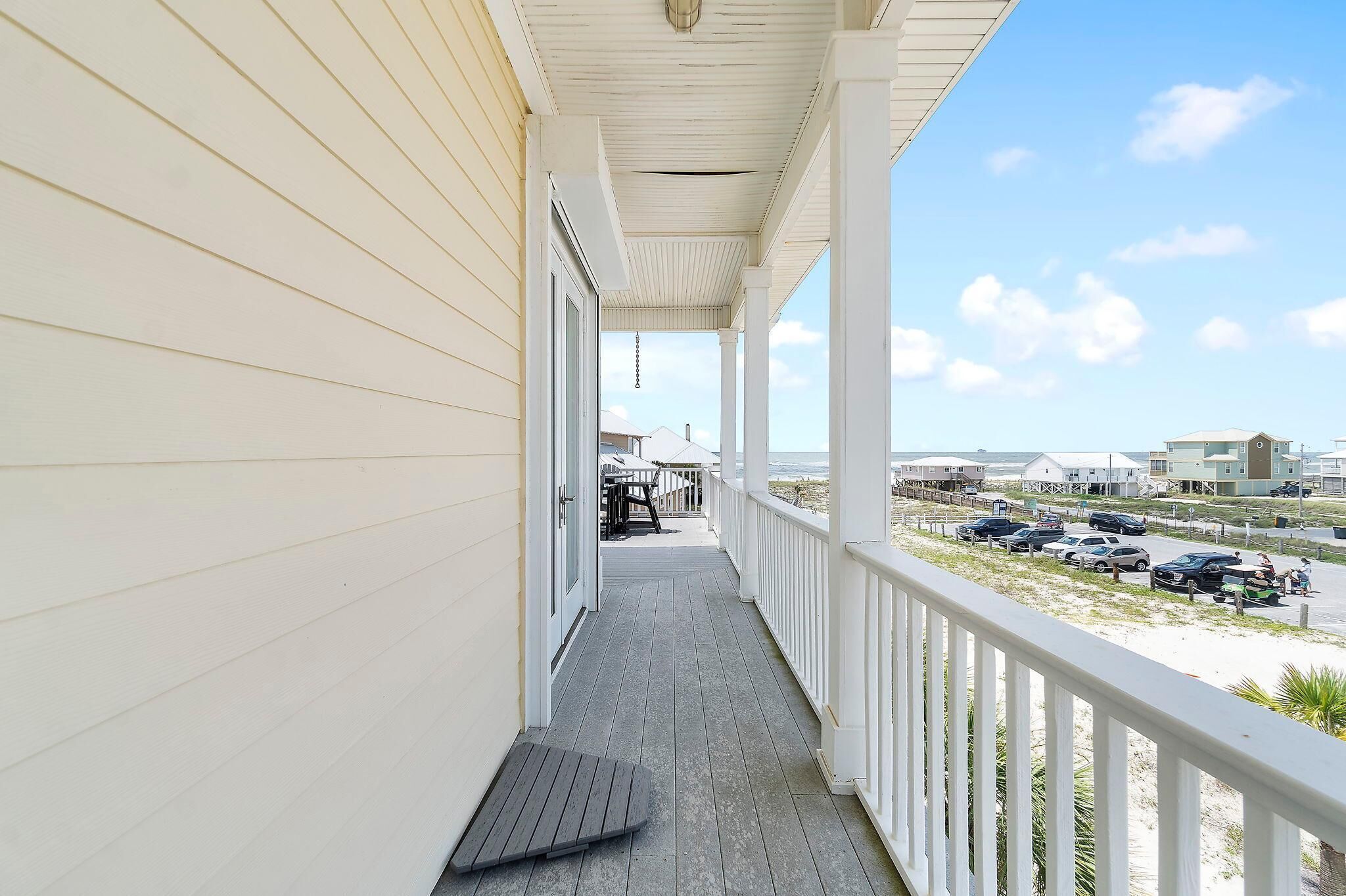 A covered balcony with a view of a parking area and beach houses.