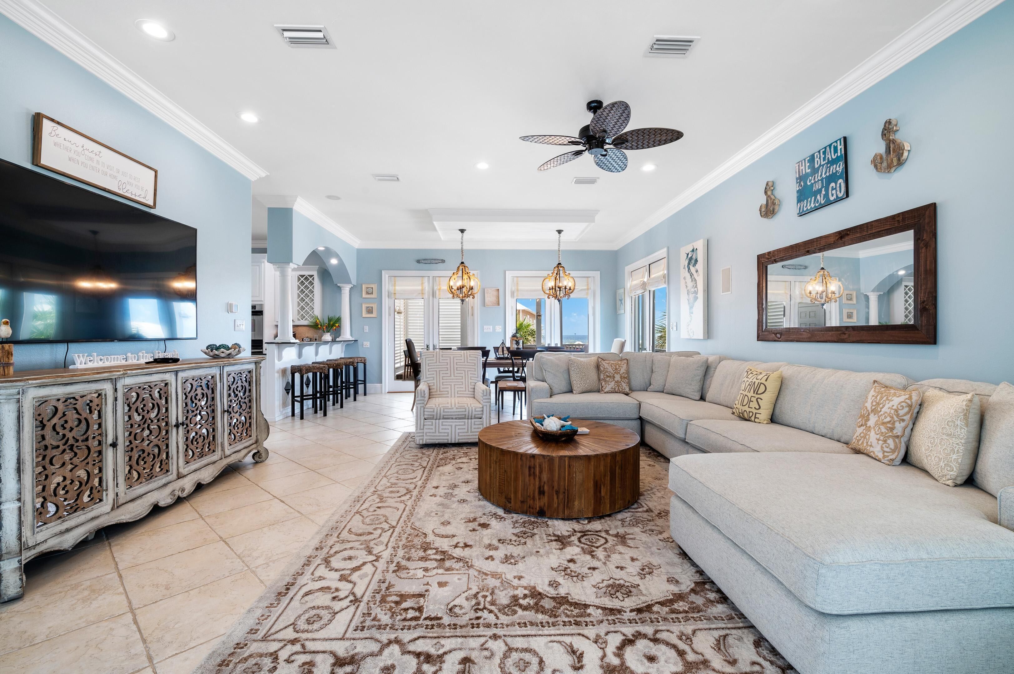 A spacious living room with a light blue wall, a large sectional sofa, a wooden coffee table, and a decorative rug.
