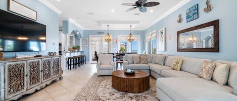 A spacious living room with a light blue wall, a large sectional sofa, a wooden coffee table, and a decorative rug.
