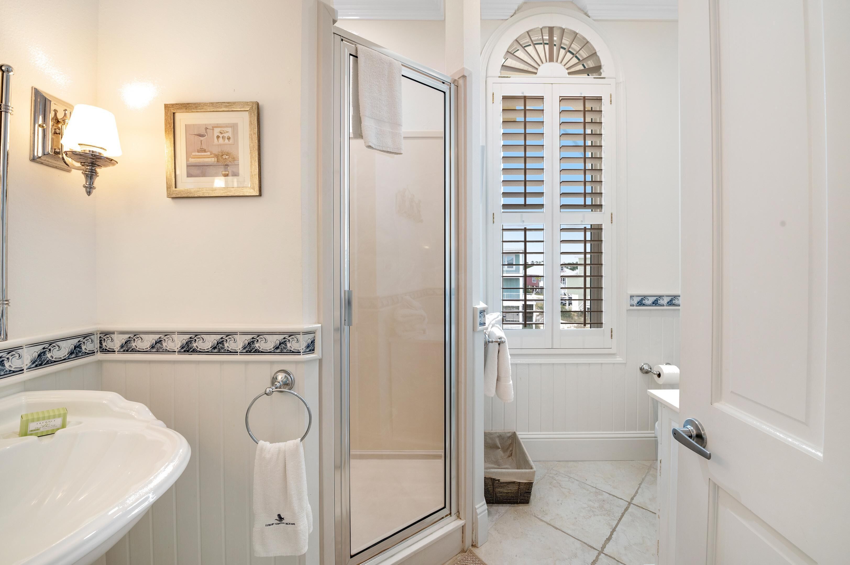A bathroom with a glass-enclosed shower, a sink with a towel ring, and a framed picture on the wall.