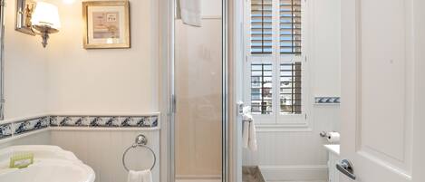 A bathroom with a glass-enclosed shower, a sink with a towel ring, and a framed picture on the wall.