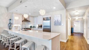 A modern kitchen with a large island, bar stools, stainless steel appliances, and pendant lighting. - Vista Del Mar 406 (Pensacola)