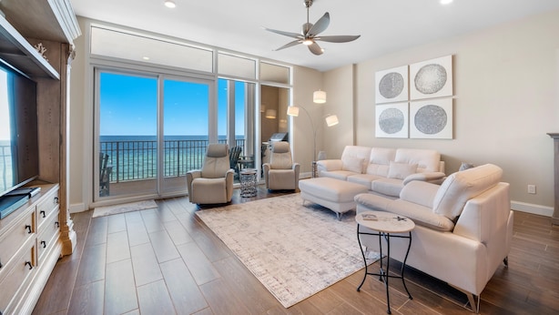 A spacious living room with a large window, a ceiling fan, and a white sofa. - Vista Del Mar 406 (Pensacola)