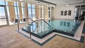 An indoor swimming pool with clear glass railings, a tiled floor, and a view of the sea through large windows. - Vista Del Mar 406 (Pensacola)
