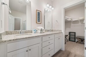 A modern bathroom with a granite countertop, a large mirror, and a walk-in shower. - Blue Angel Casa (Pensacola)