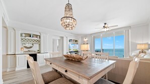 Zona pranzo con tavolo e sedie in legno, un lampadario e vista sull'oceano.