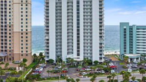 A high-rise hotel with multiple balconies, a parking lot, and a view of the ocean. - Palacio 1804 (Pensacola)