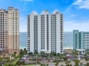A high-rise hotel with multiple balconies, a parking lot, and a view of the ocean. - Palacio 1804 (Pensacola)
