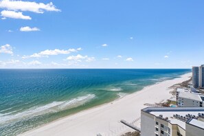 A beach view with a clear sky, a sandy shore, and a building with multiple floors. - Palacio 1804 (Pensacola)