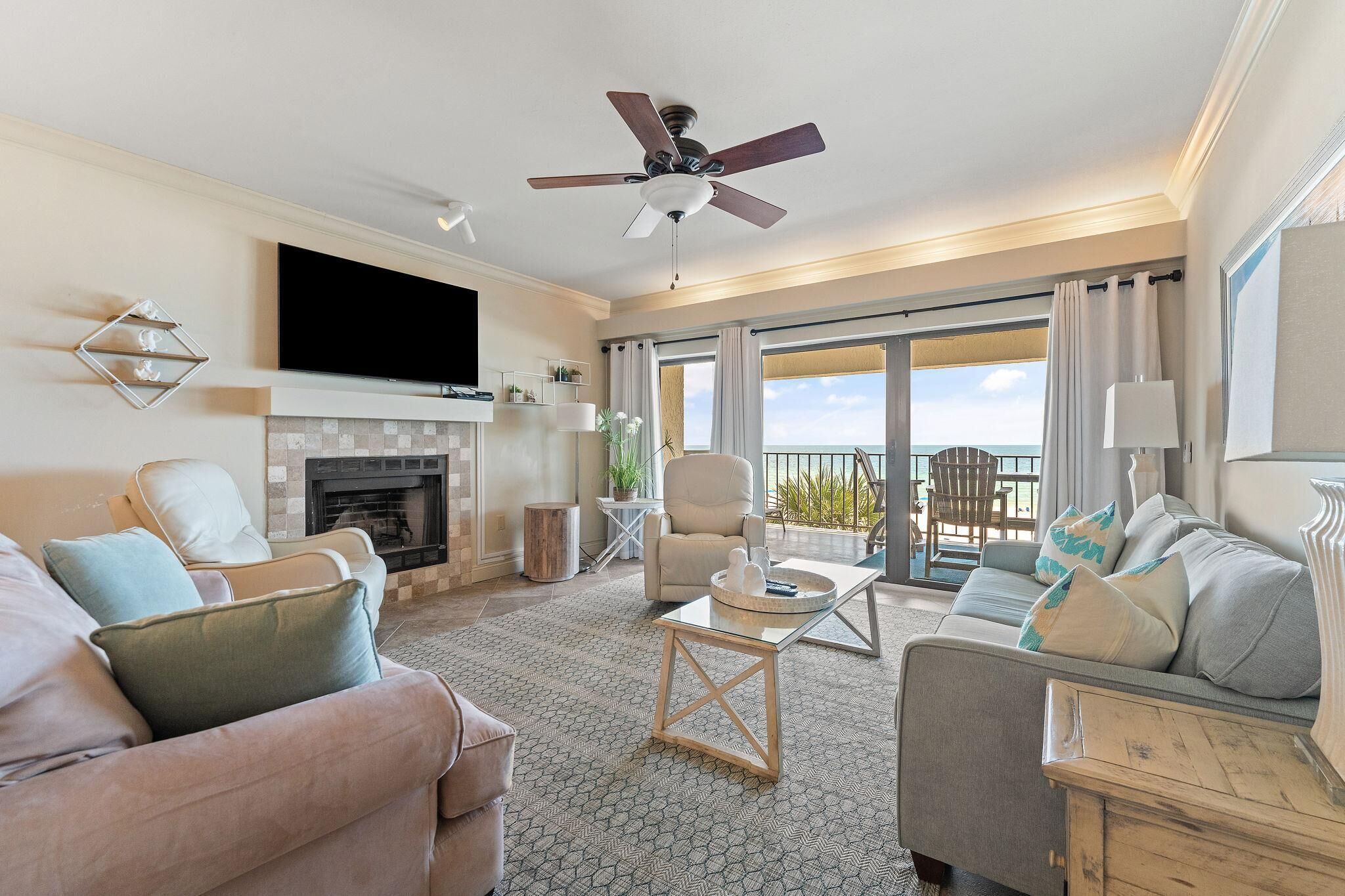 A spacious living room with a fireplace, a ceiling fan, and a large TV. There are two sofas and a coffee table.