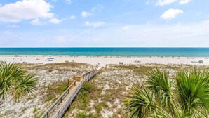 A beach with a wooden boardwalk leading to the shore, sandy dunes, and a clear blue sky. - Shipwatch D401 (Pensacola)