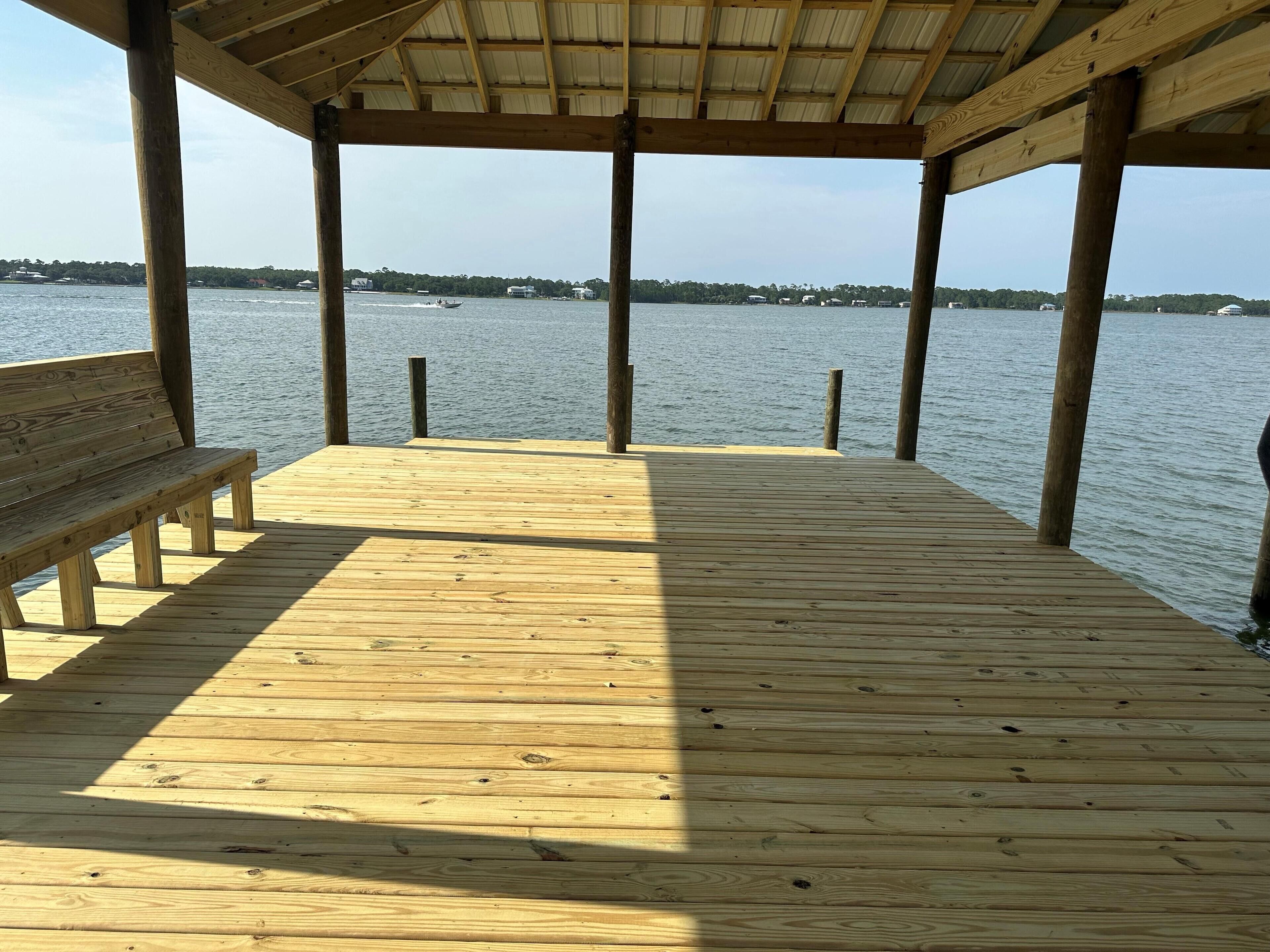 A wooden pier with a bench, leading to a body of water with boats and buildings in the background.