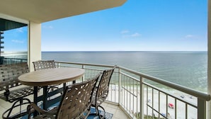 A balcony with a table and chairs, overlooking a beach and the ocean. - Indigo East 1502 (Pensacola)