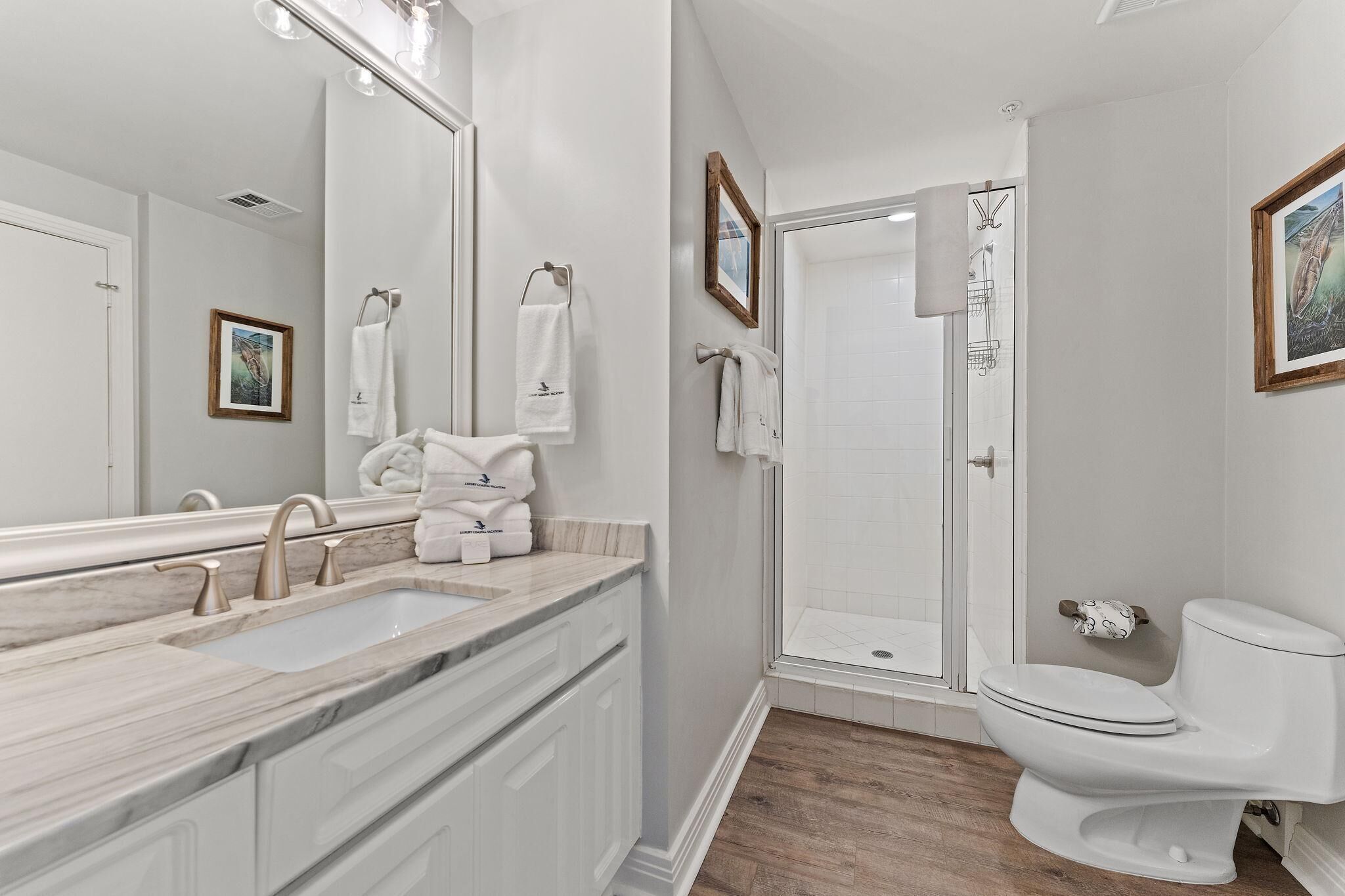 A modern bathroom with a marble sink, a toilet, and a glass shower enclosure.