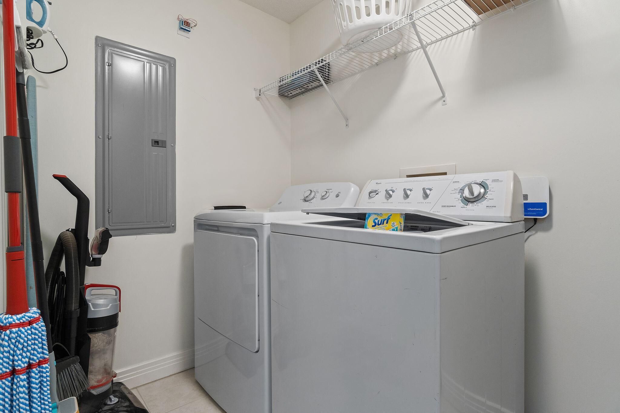 A laundry area with a front-loading washer and dryer, a vacuum cleaner, and a storage basket.
