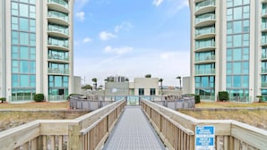A wooden walkway leading to a modern building with balconies and large windows.