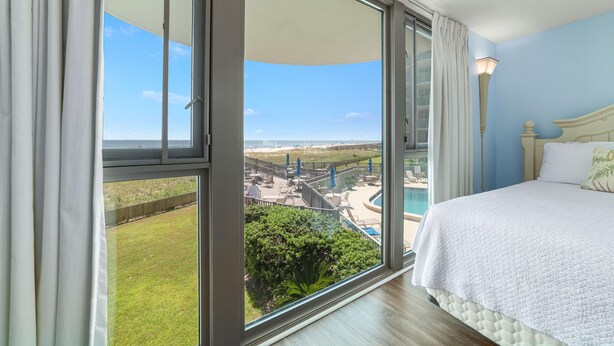 A bedroom with a large window, a bed, and a view of a pool and beach.