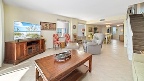 A spacious living room with a wooden coffee table, a flat-screen TV, and a dining area with chairs and a table.