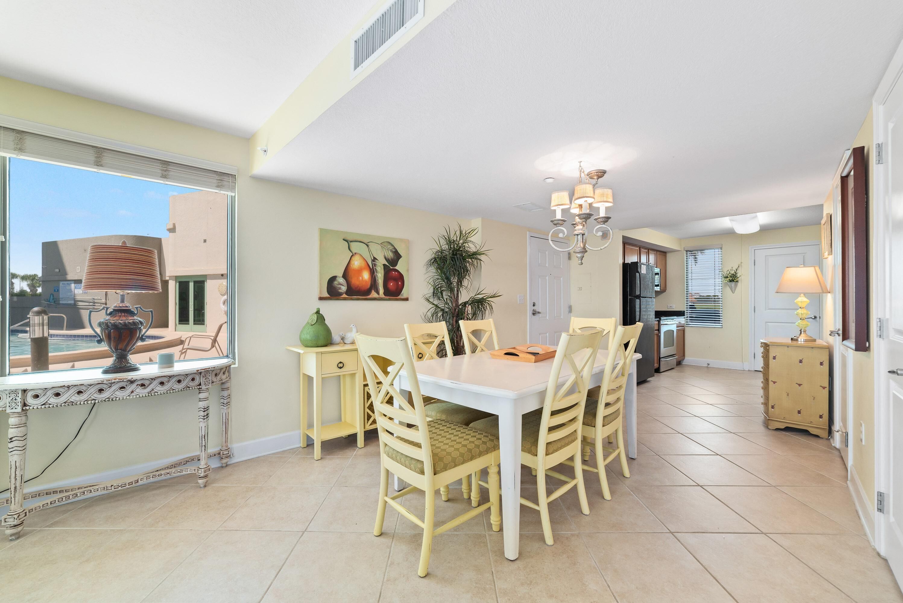 A dining area with a white table and chairs, a chandelier, and a painting of fruits on the wall.