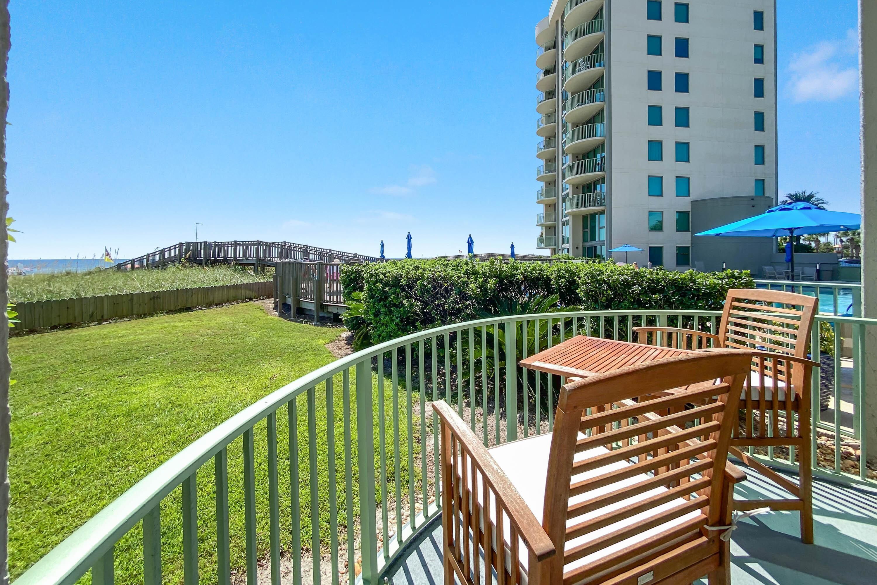 A balcony with a view of a grassy area, a wooden fence, and a tall building in the background.