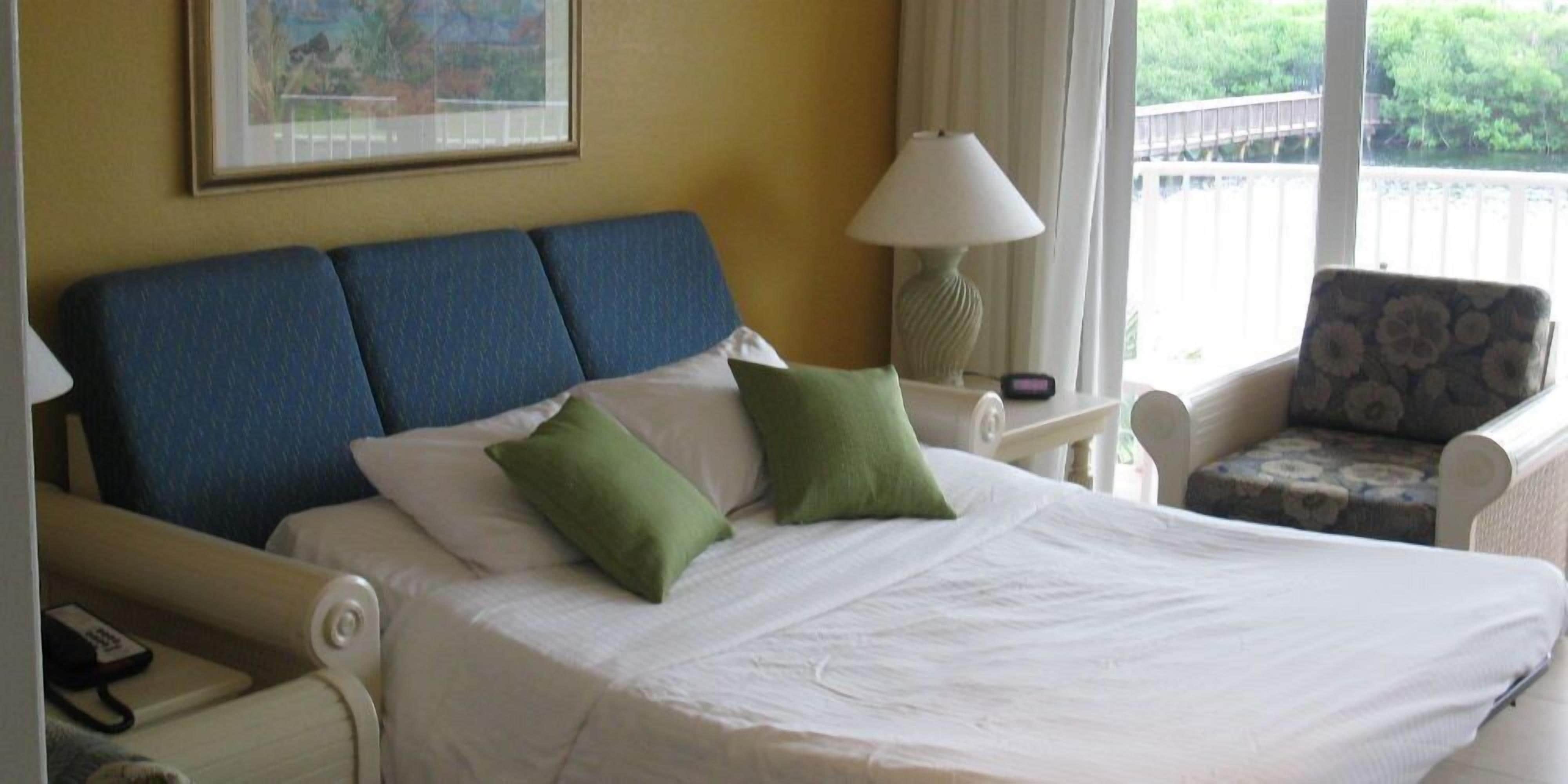 Une chambre d’hôtel avec un lit, une chaise, une lampe et une fenêtre donnant sur un paysage verdoyant.